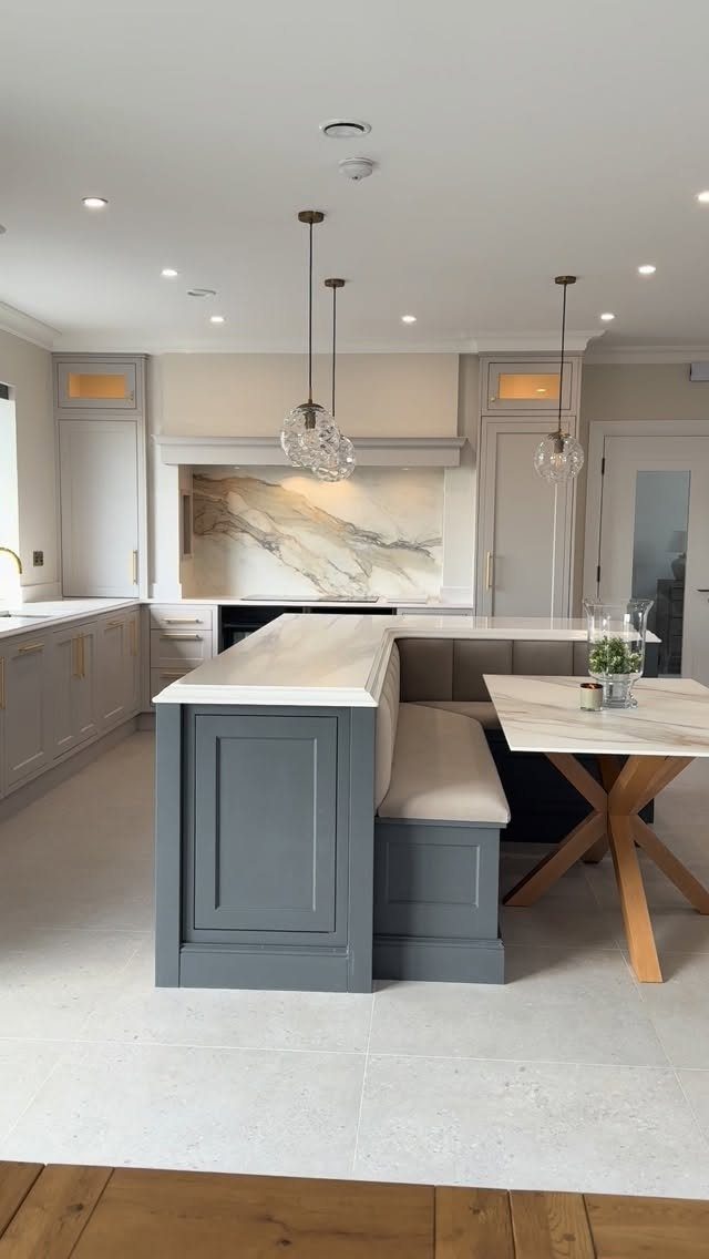 Grey kitchen island with integrated banquette seating and a marble dining table