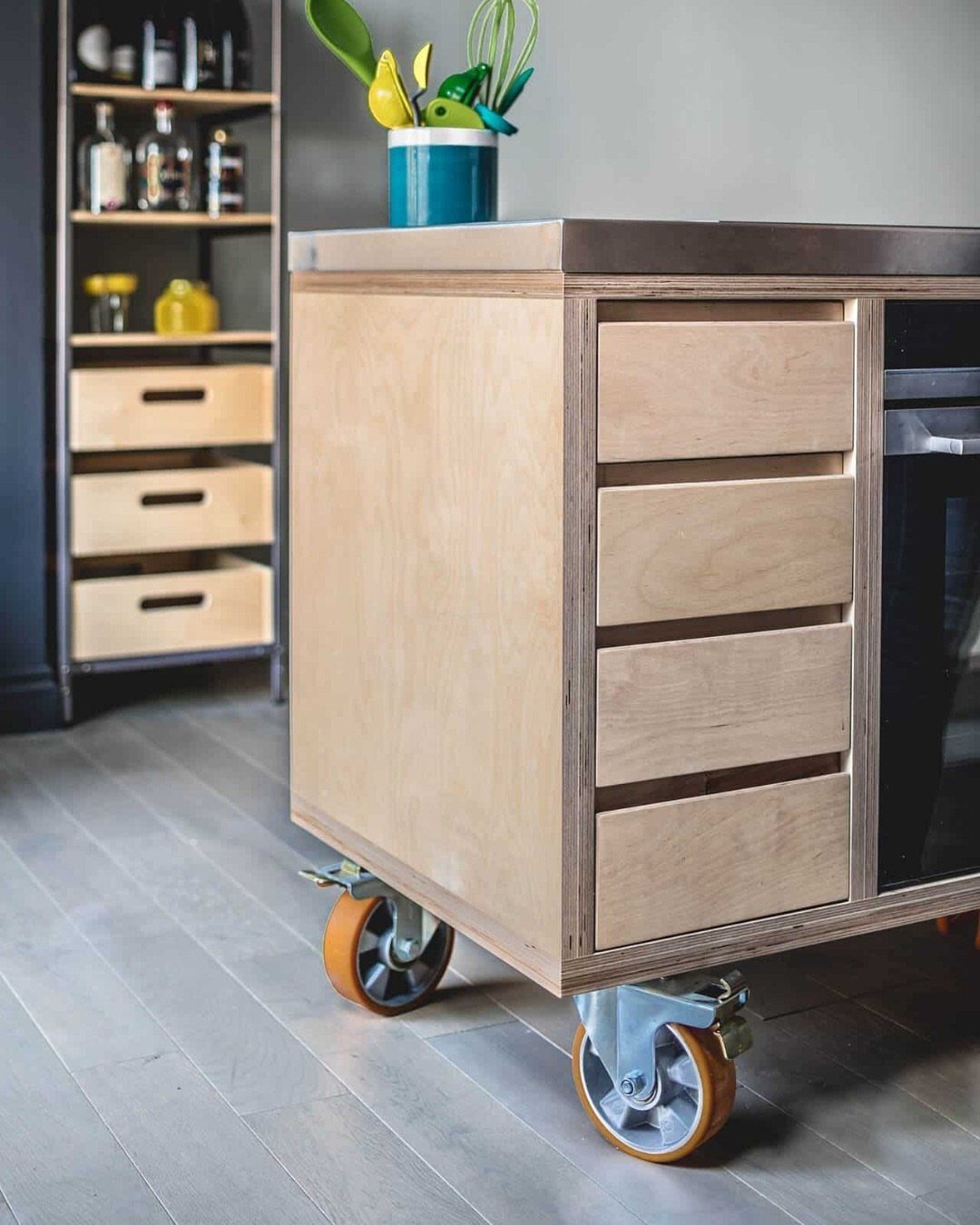 Wooden kitchen island with drawers and orange caster wheels on a grey floor