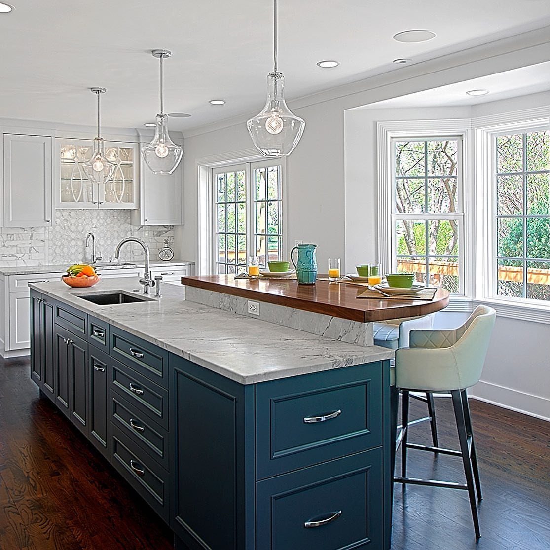 Blue kitchen island with white marble counter and raised wooden dining level.