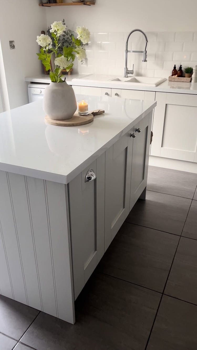 Small light grey kitchen island with white countertop and white floral arrangement
