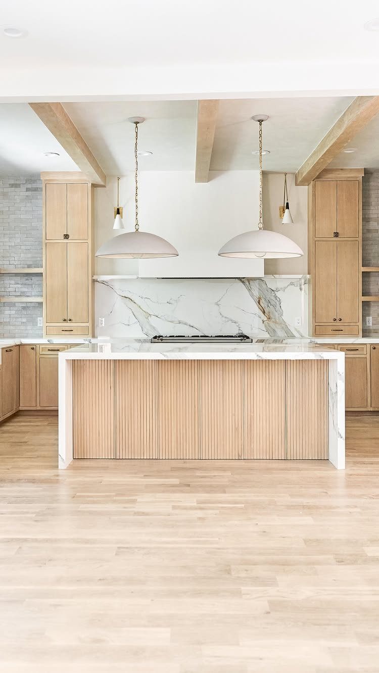 White marble waterfall-edge kitchen island with light wood slatted base and pendant lighting.