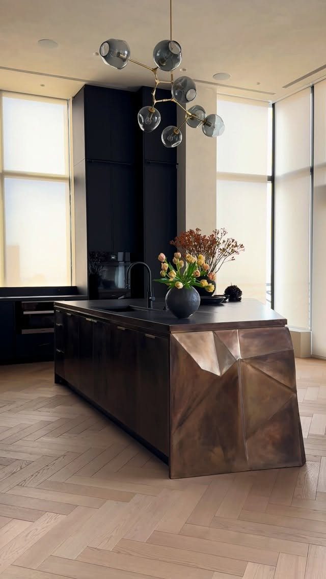 Modern kitchen island with a faceted metallic back panel and herringbone wood floors.