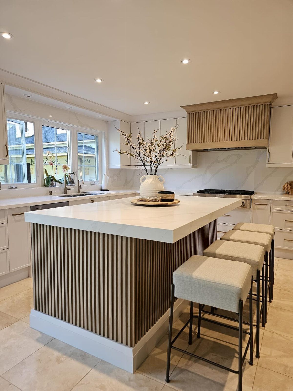 Kitchen island with light wood fluted panels and beige upholstered bar stools.