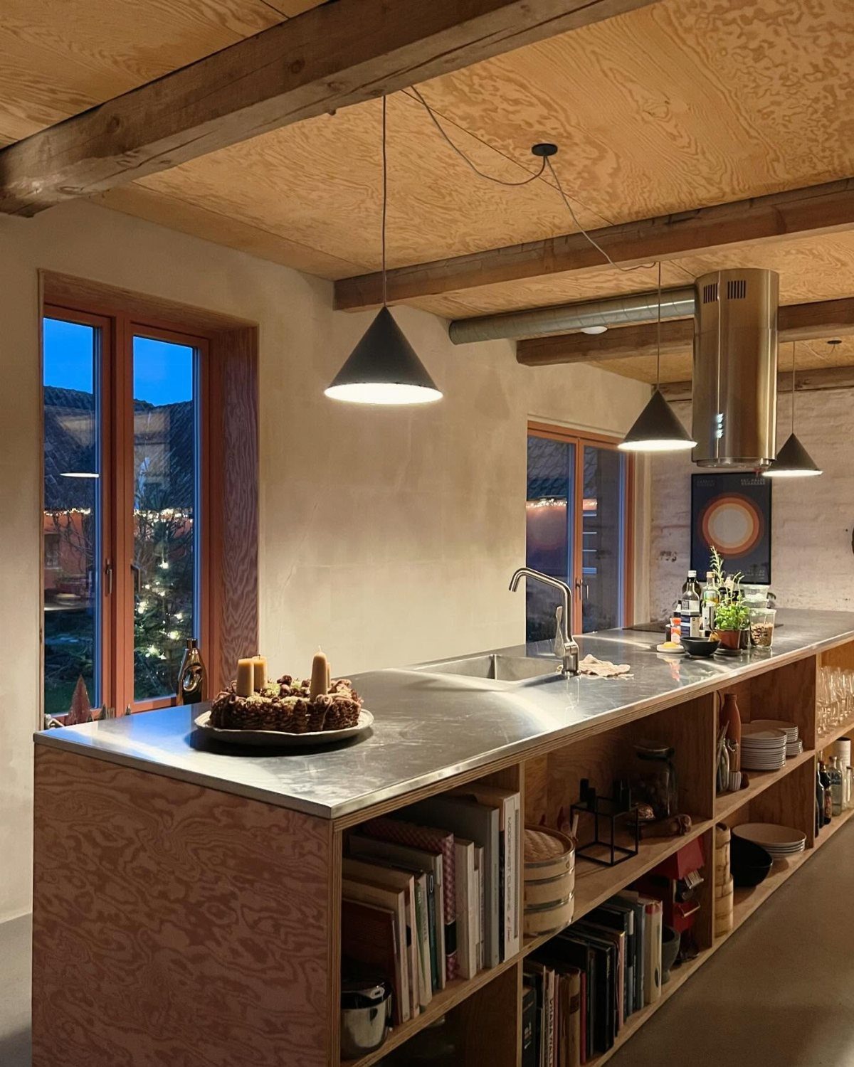 Plywood kitchen island with metal countertop and open shelving under wooden beams