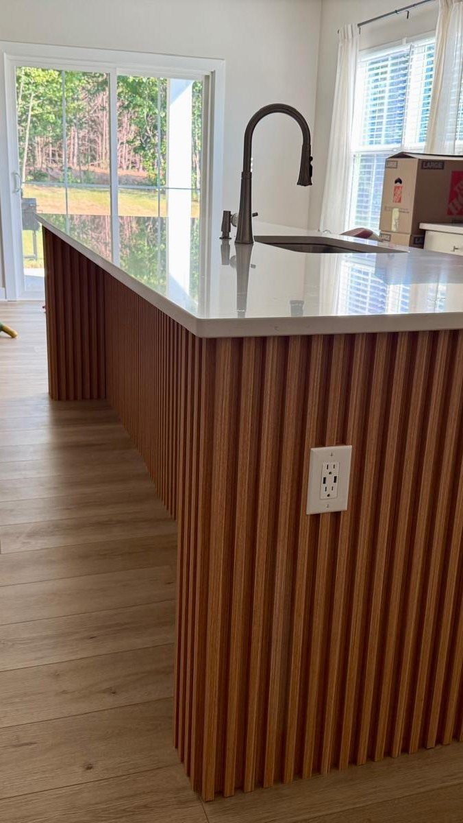 Kitchen island with a white countertop and vertical wooden slat back paneling.