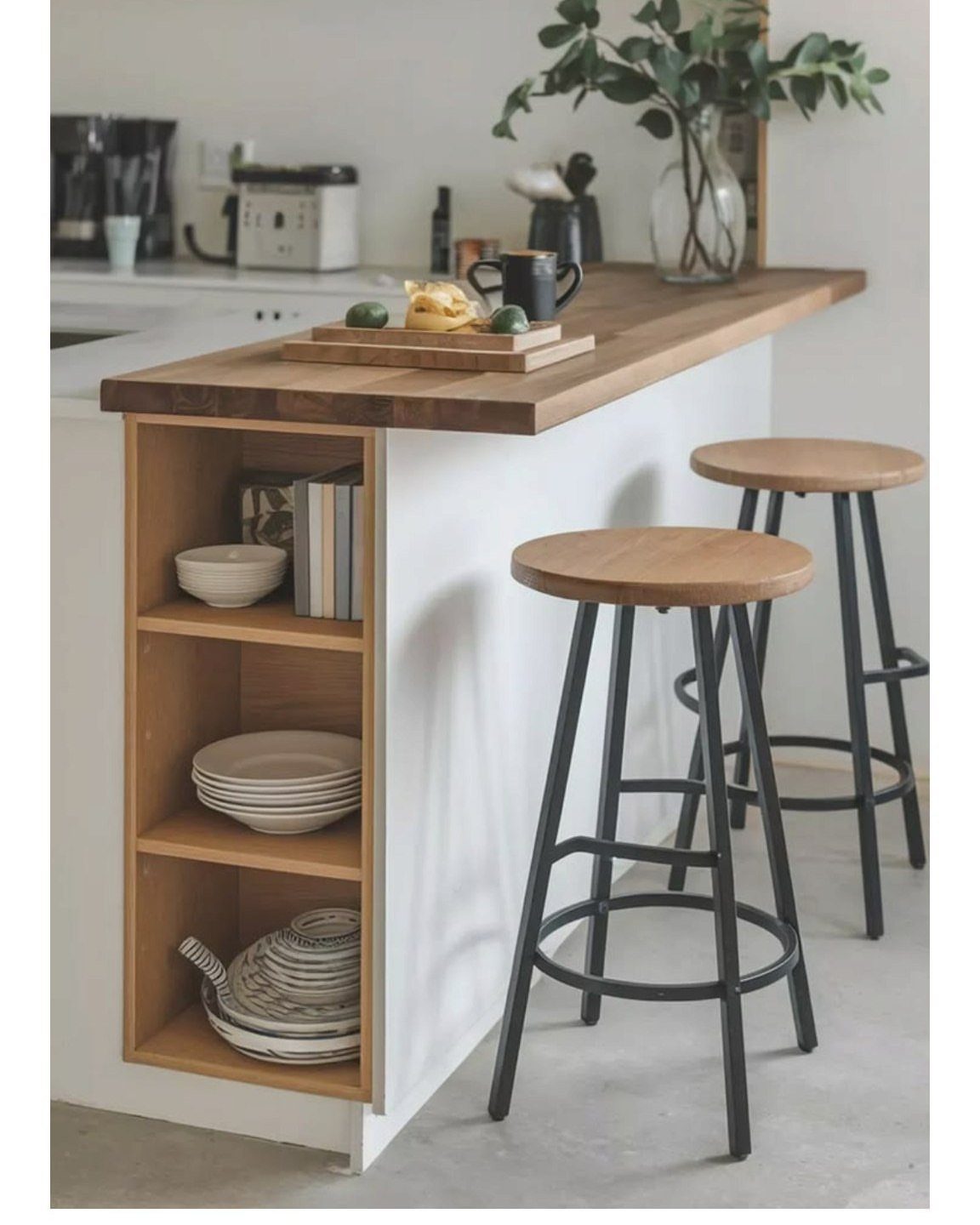 White kitchen island with wooden countertop, open shelving, and two wooden bar stools.