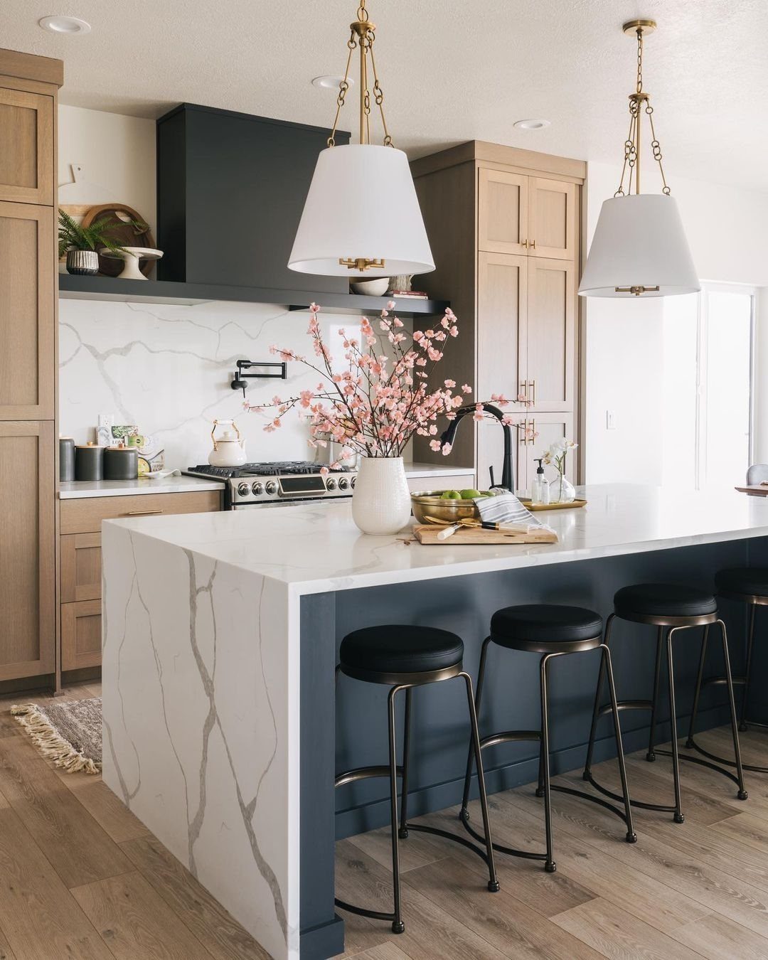 White marble kitchen island with navy blue base and four black bar stools.