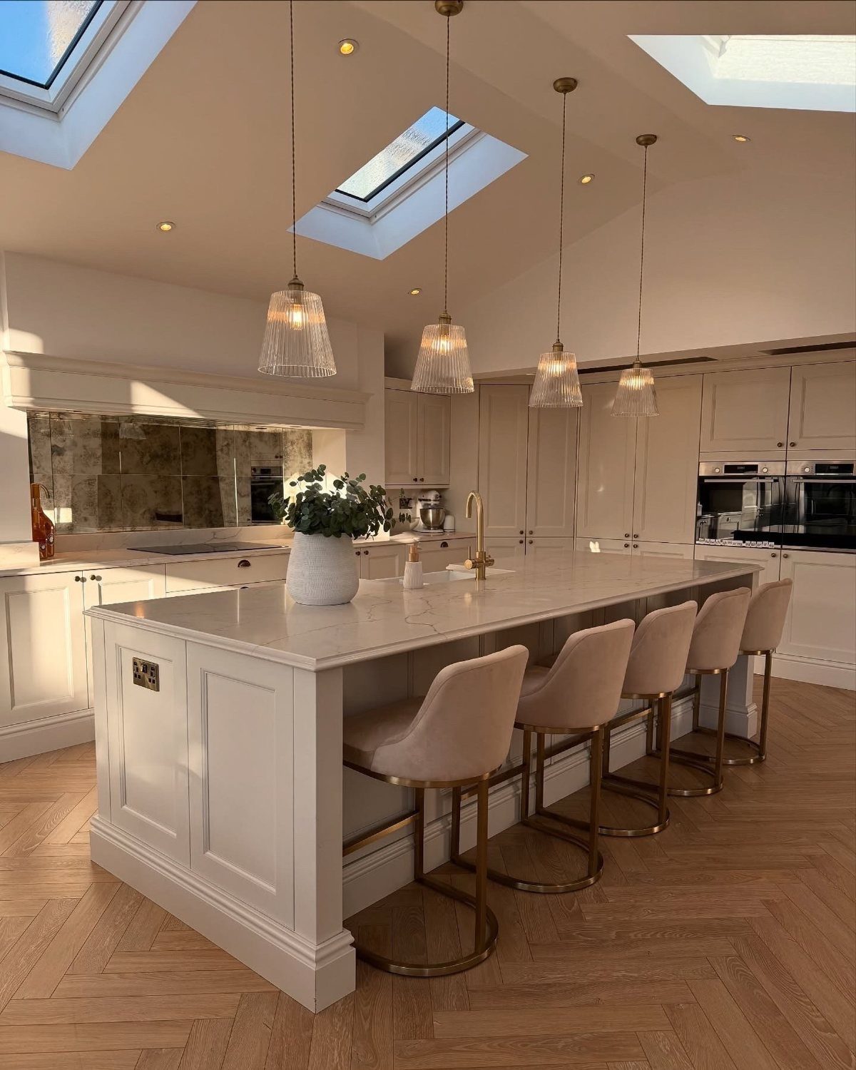 White kitchen island with beige bar stools and four glass pendant lights hanging above.