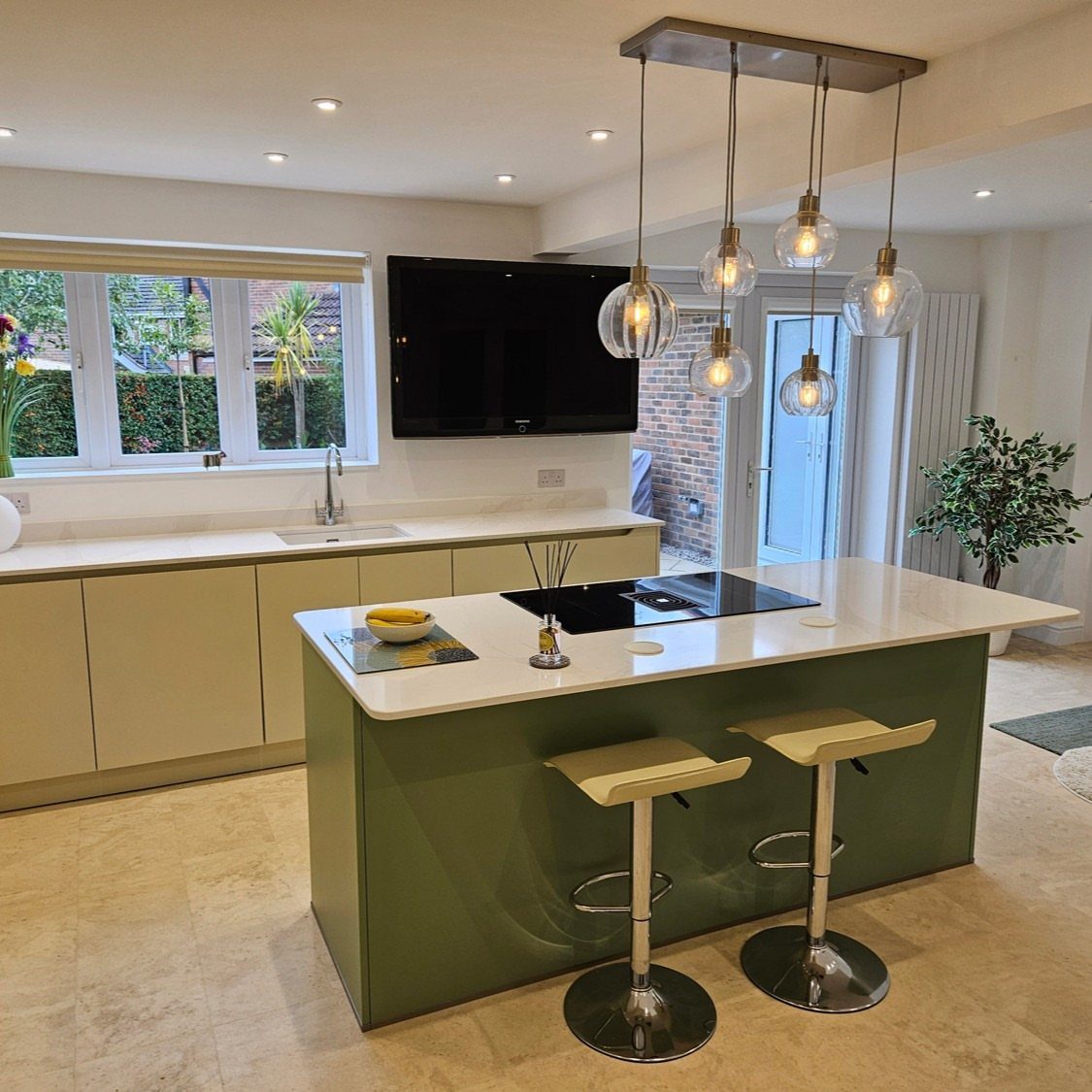 Green kitchen island with white countertop and two yellow bar stools under pendant lights