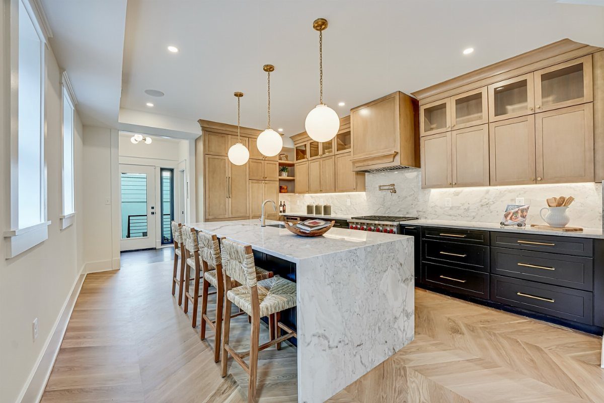 White marble waterfall kitchen island with four upholstered stools and spherical pendant lights.