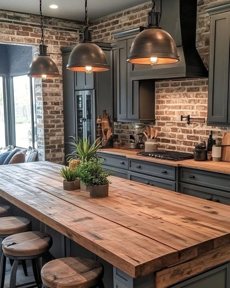 Wooden kitchen island with leather stools under industrial pendant lights and brick walls