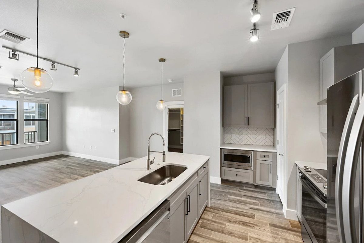 White marble kitchen island with a stainless steel sink and modern pendant lighting.