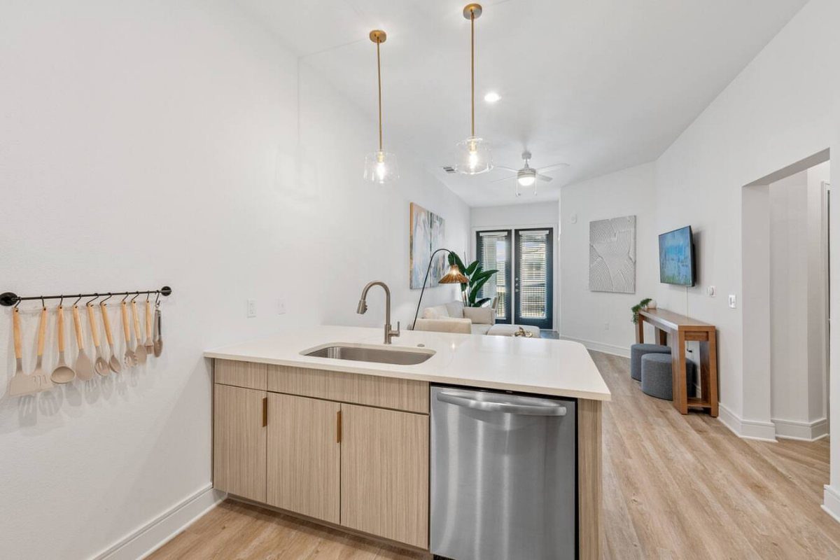 Kitchen island with white countertop, stainless steel sink, and light wood cabinetry.