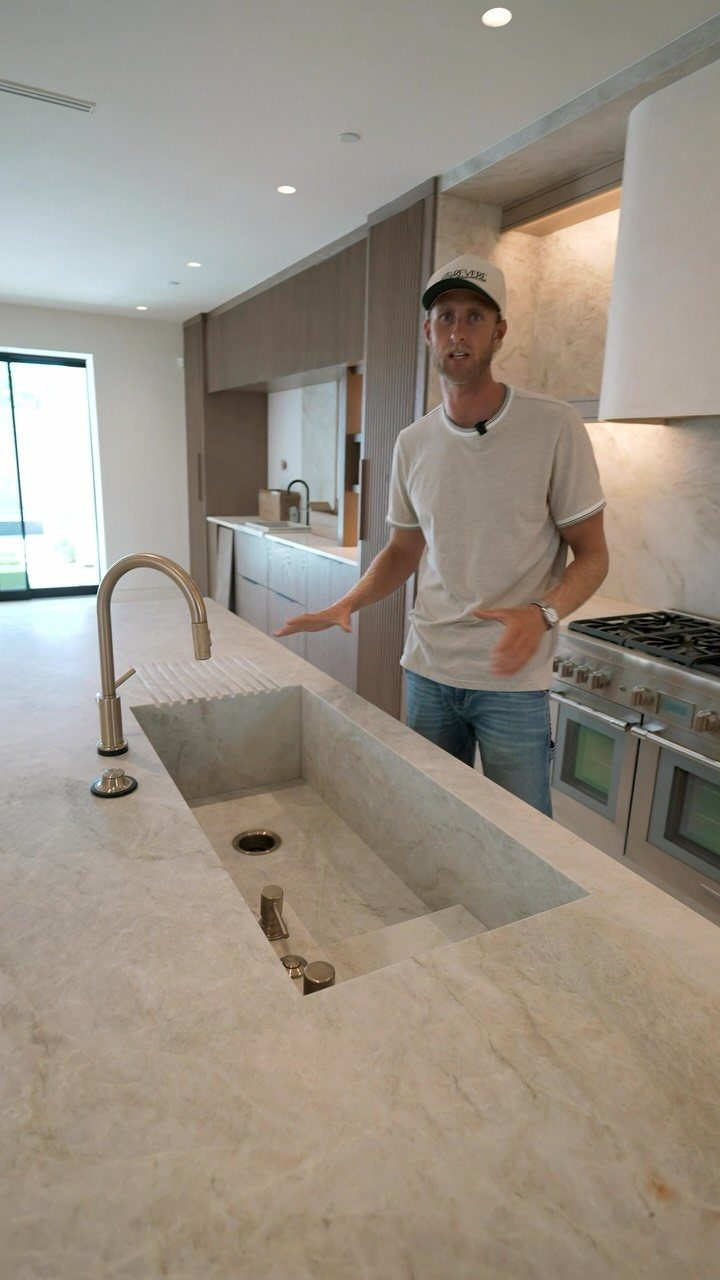 Man standing by a modern stone kitchen island with an off-center integrated sink.