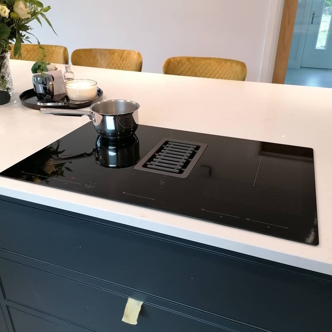 Black induction cooktop with a stainless steel pot on a white kitchen island.