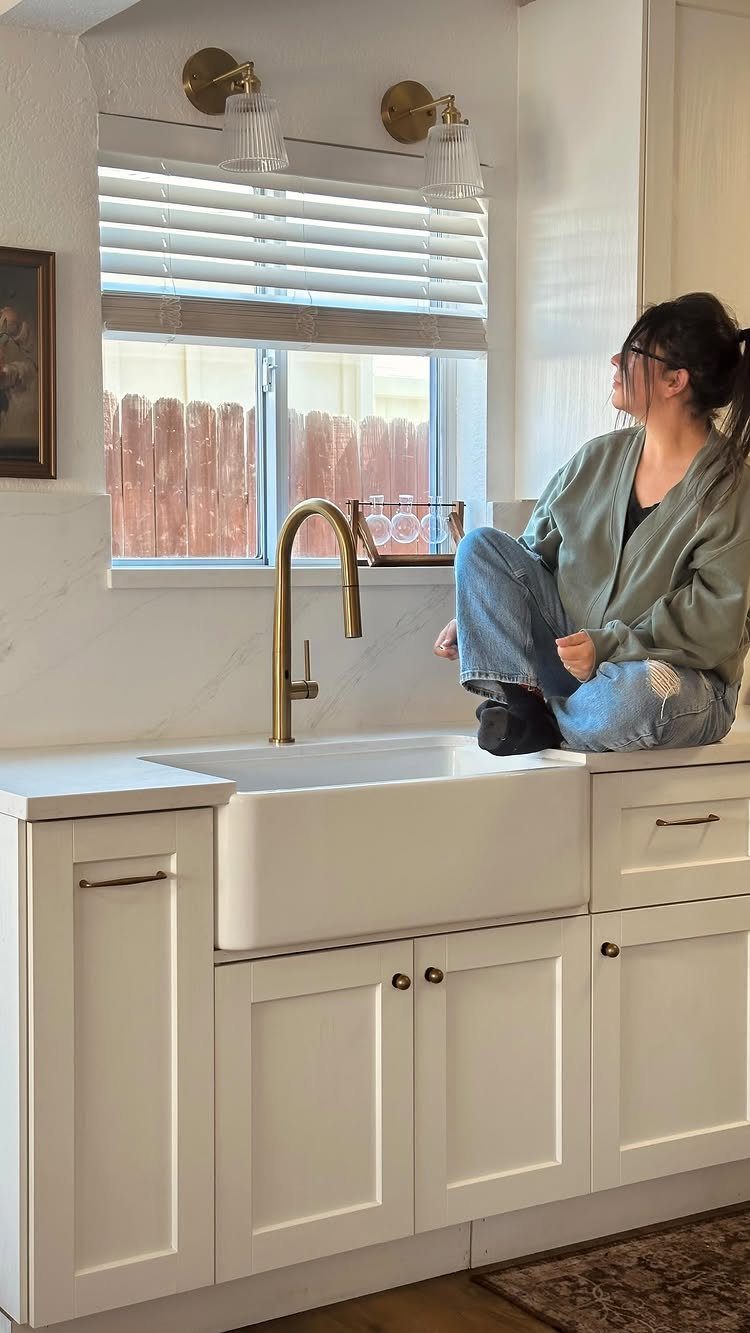 Gold wall sconces mounted above a white farmhouse sink in a bright kitchen.