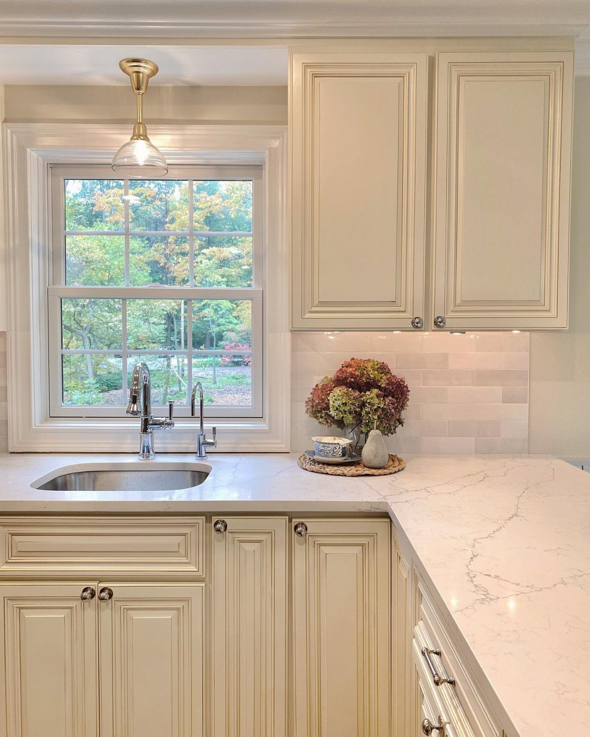 Gold pendant light hanging over a kitchen sink with white cabinets and marble countertops