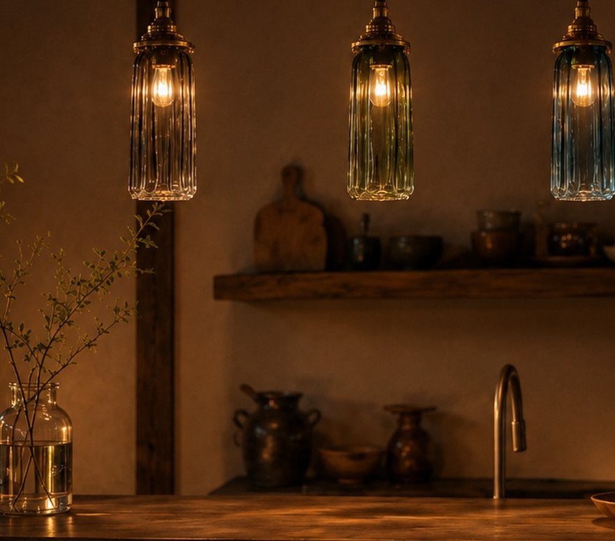 Three ribbed glass pendant lights glowing warmly over a rustic kitchen sink area.