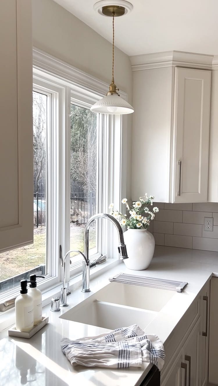 White pendant light hanging over a kitchen sink in front of a window