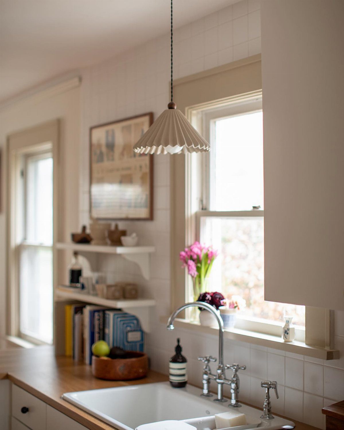 White pleated pendant light hanging over a white kitchen sink by a window