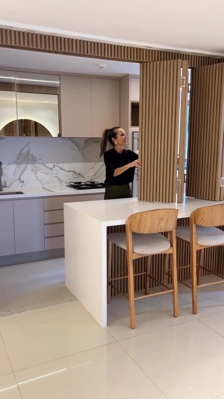 Modern kitchen with white island, wooden bar stools, and vertical slat room divider.