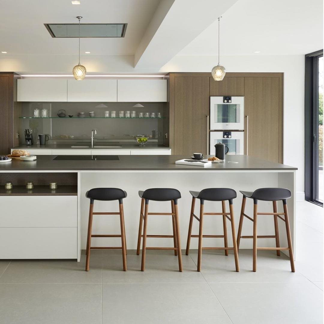 Modern kitchen island with black bar stools, white cabinets, and wood paneling.