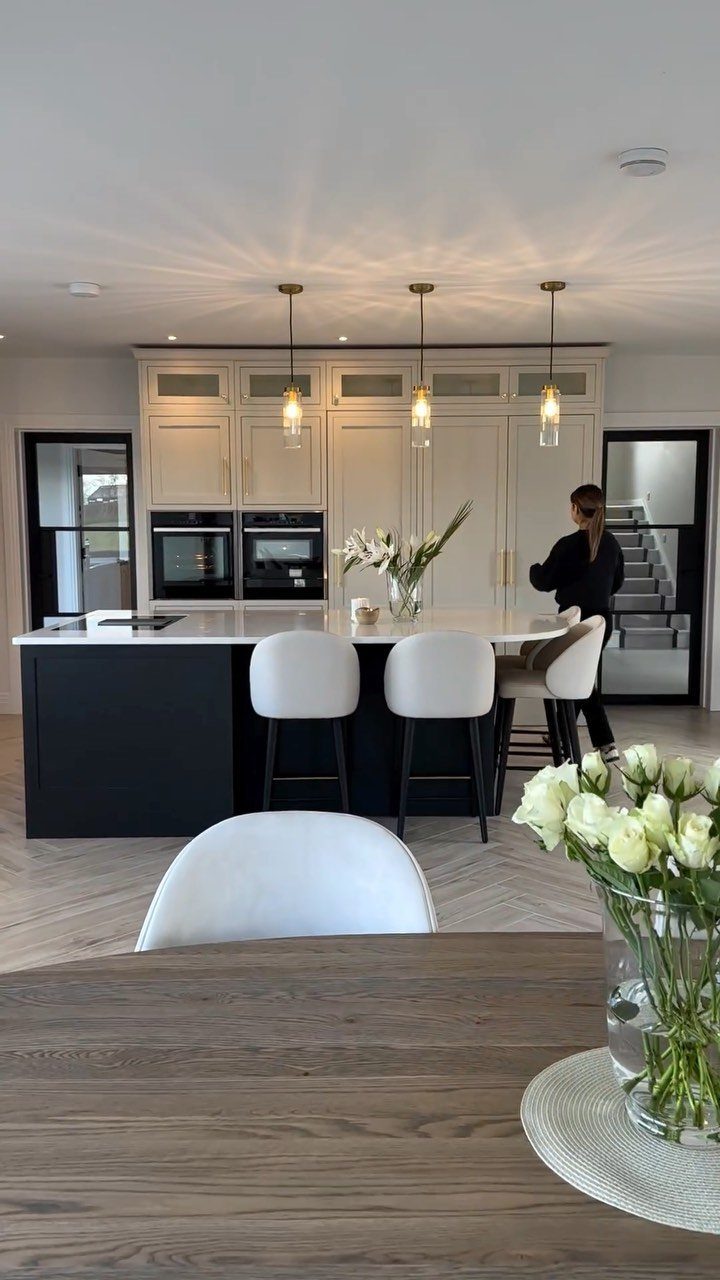 Black kitchen island with white countertop and three white bar stools in modern room