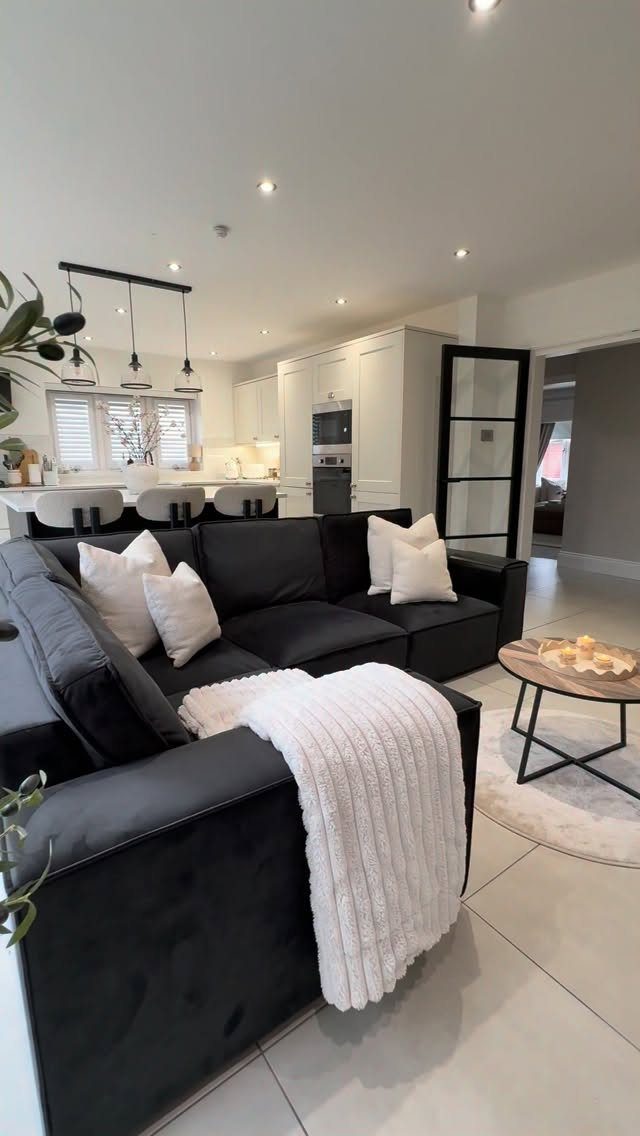 Black sectional sofa in a living room opening into a white modern kitchen.