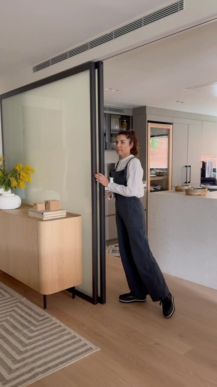 Woman standing by a sliding glass door separating a living area from a kitchen.