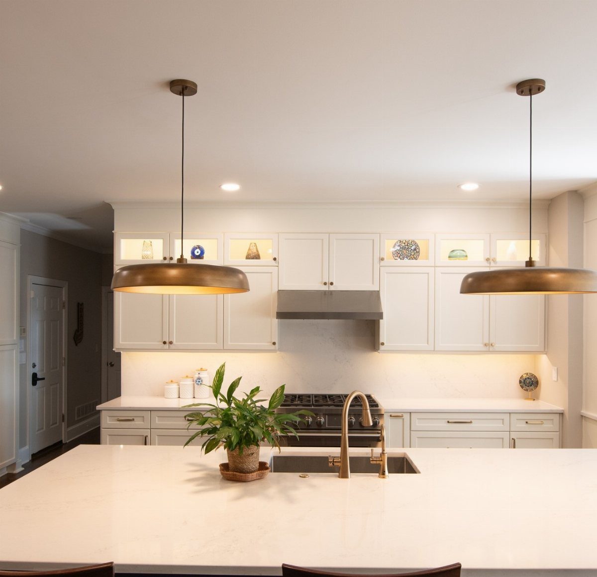 White kitchen cabinets and marble island with bronze pendant lighting and a plant.