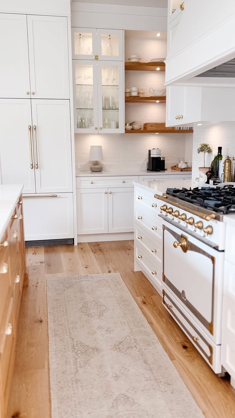 White kitchen cabinets and stove with gold hardware on light wood floors.