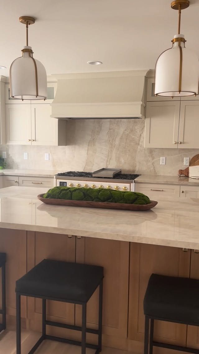 Off-white kitchen cabinets and marble island with black barstools and pendant lighting.