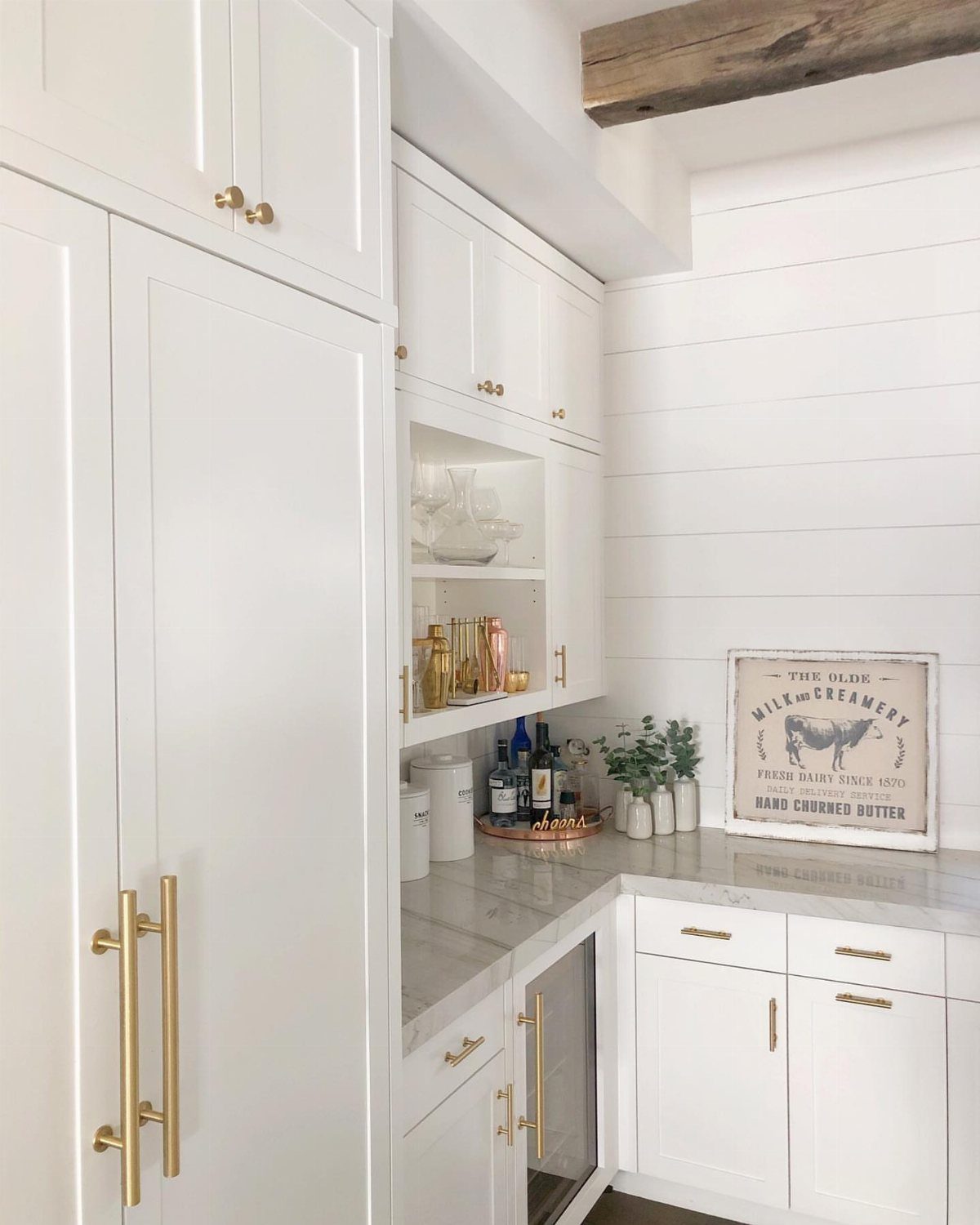 White kitchen cabinets with gold handles and a white shiplap wall background.