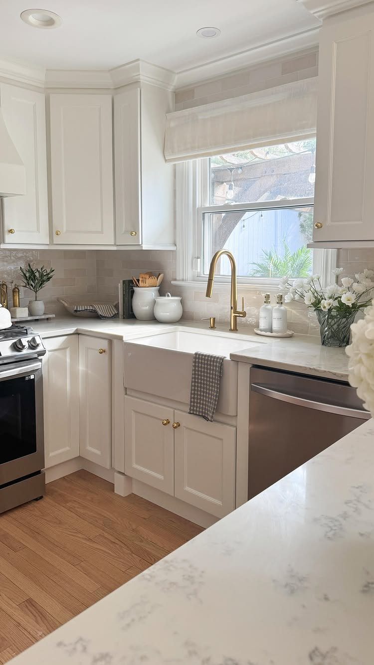 Creamy off-white kitchen cabinets with a farmhouse sink and gold faucet hardware.