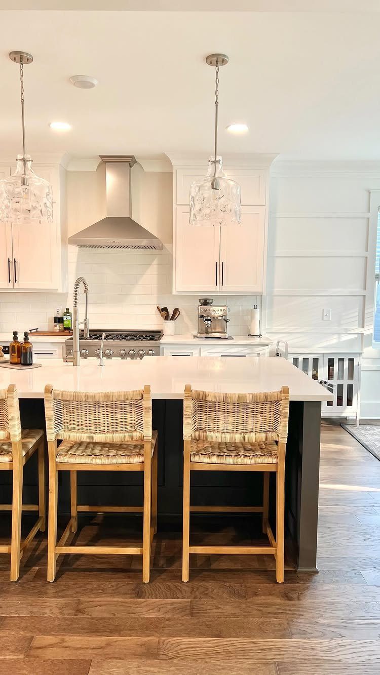 White kitchen cabinets and a dark grey island with woven wicker bar stools.