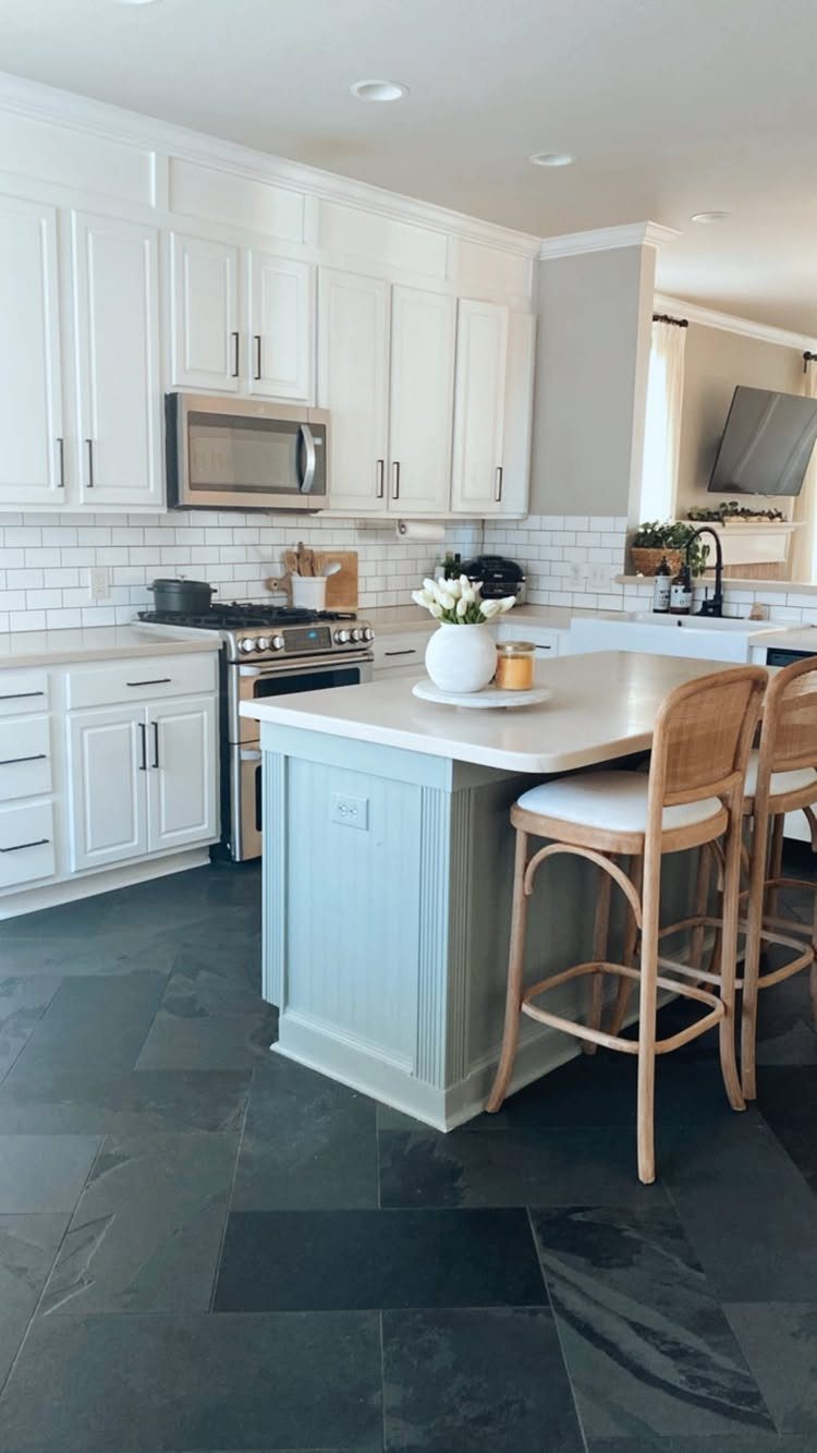 White kitchen cabinets and a sage green island with wooden bar stools.