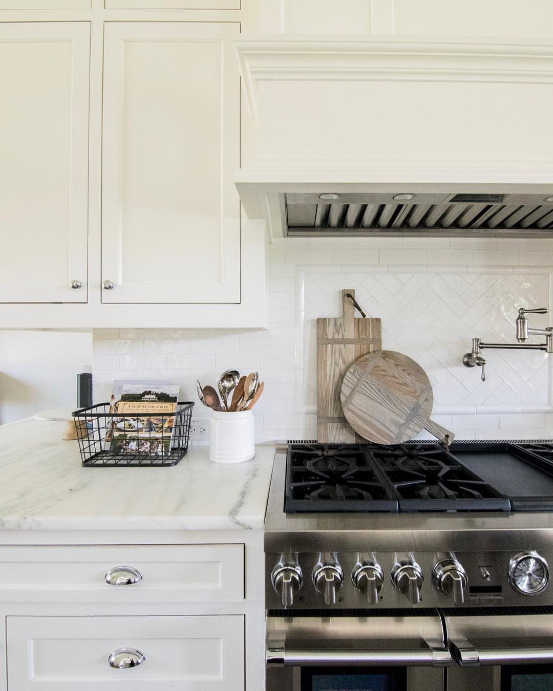 Off-white kitchen cabinets with marble countertops and a professional stainless steel gas range.