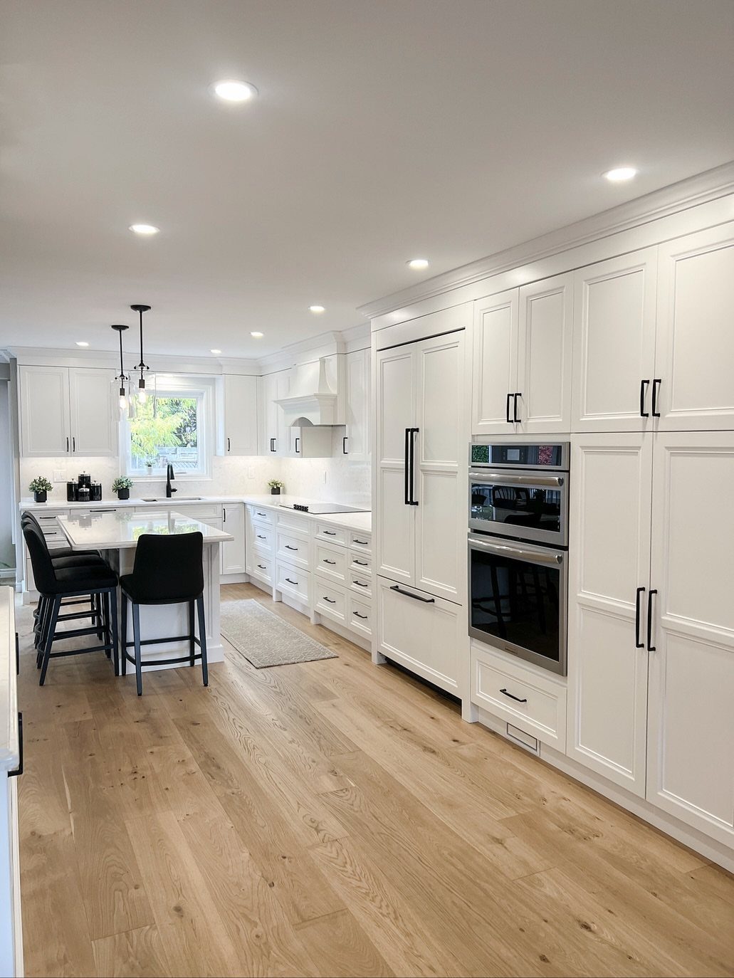White shaker cabinets with black handles in a bright kitchen with light wood floors.