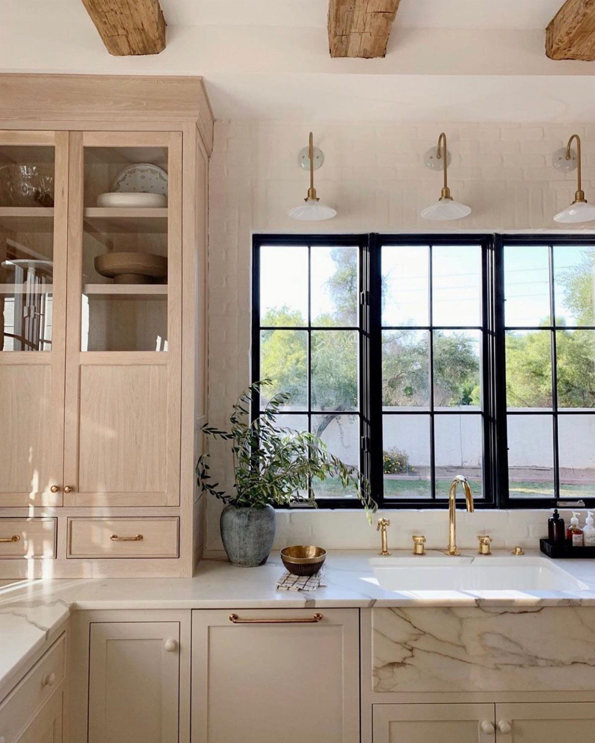 White marble farmhouse sink with gold faucet in a bright, rustic kitchen