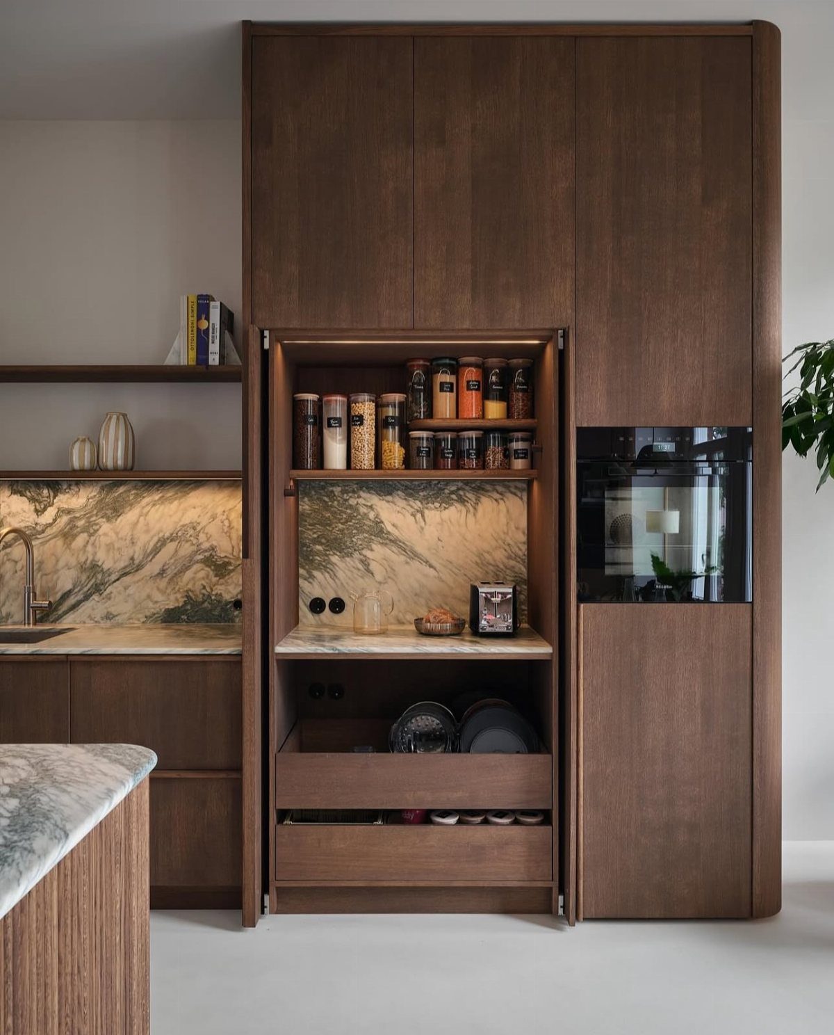 Dark textured wood kitchen cabinets with a marble backsplash and organized pantry storage.