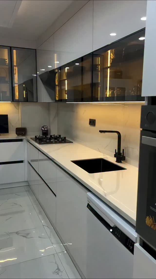 Modern white kitchen with glossy cabinets, black fixtures, and white marble flooring.