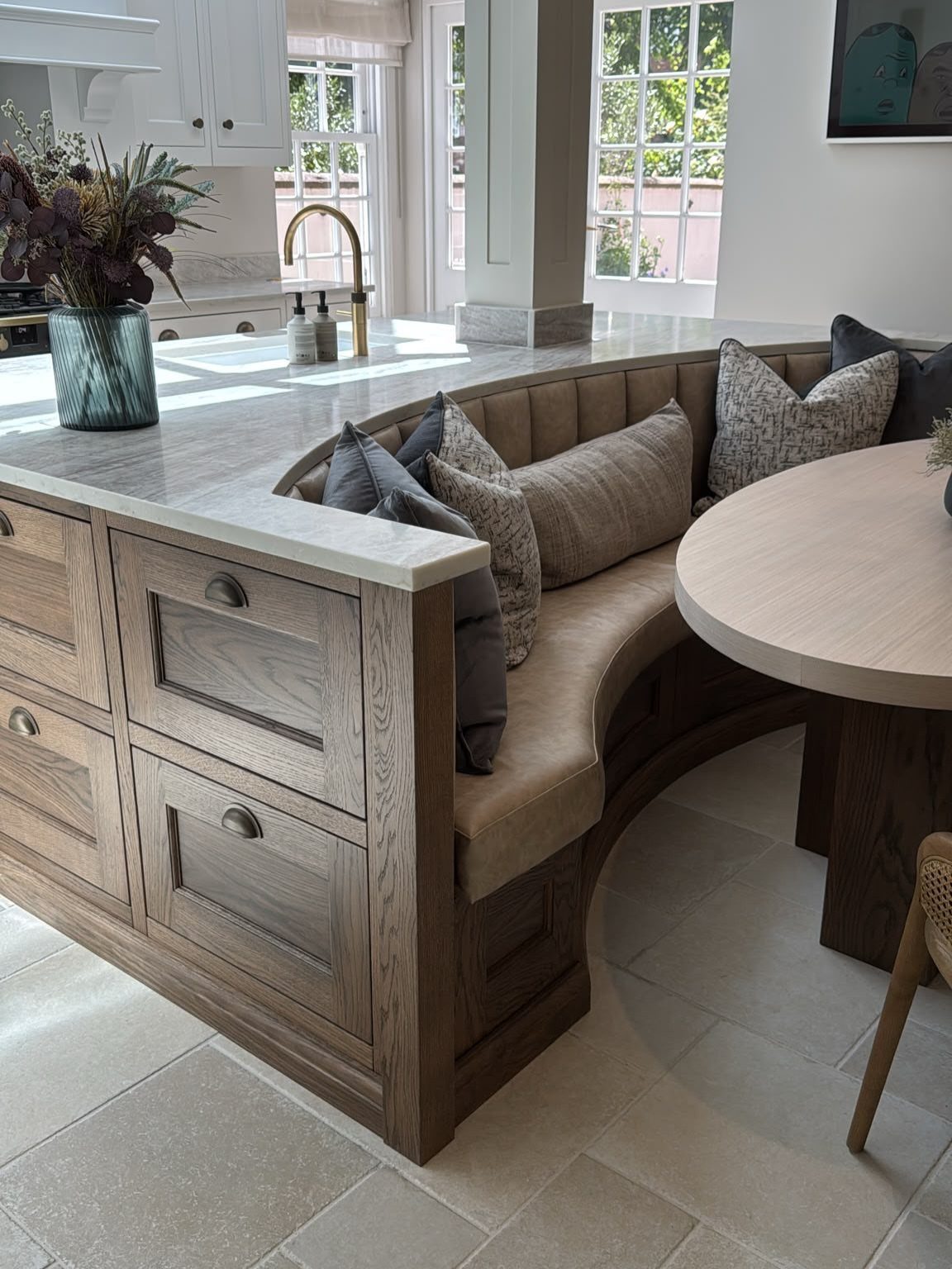 Curved built-in bench seating nook with tan cushions and a round wooden table.