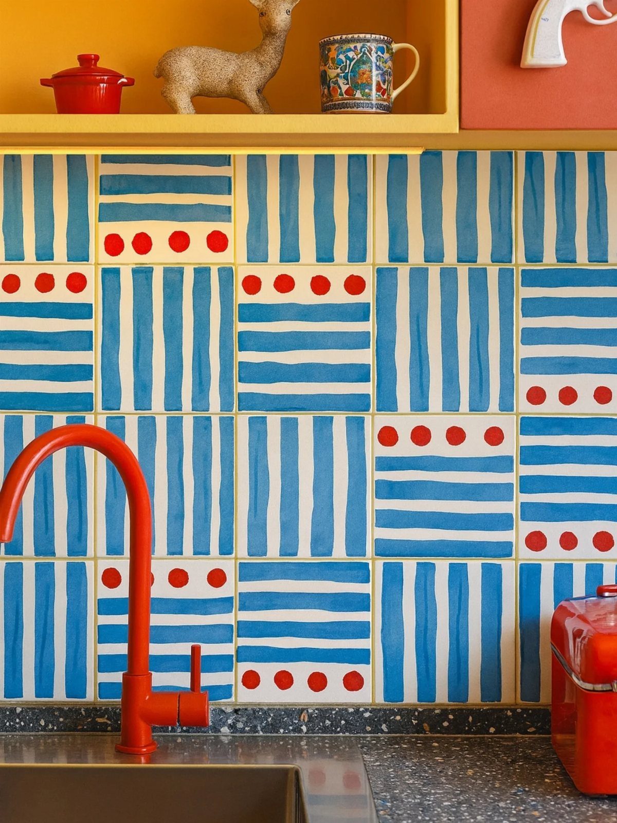 Bold blue and red patterned tiles on a kitchen backsplash with a red faucet.
