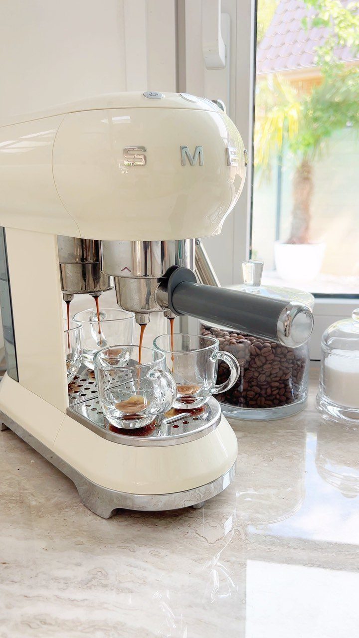 Cream espresso machine brewing coffee into glass cups on a marble countertop