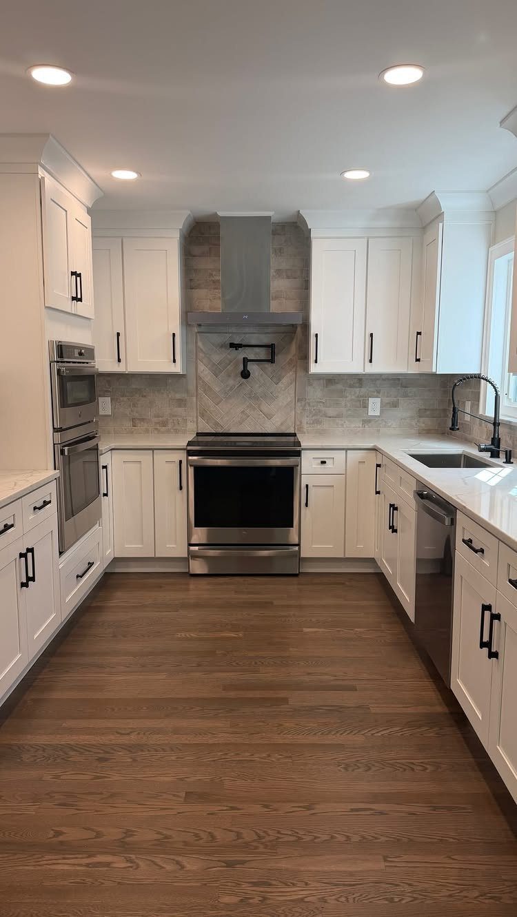 White galley kitchen with stainless steel appliances and brown wood floors.