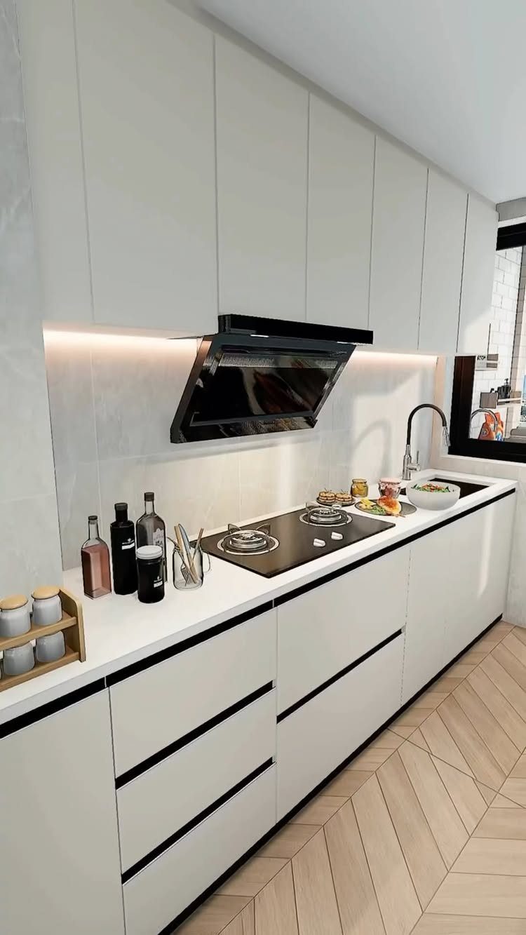 Modern small kitchen with white cabinets, black stovetop, and herringbone wood floors.