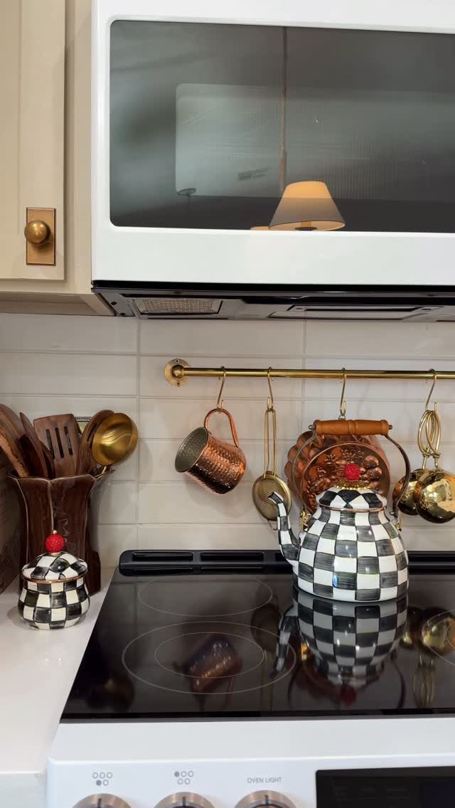 Gold hanging rail with copper mugs and utensils above a black stovetop.