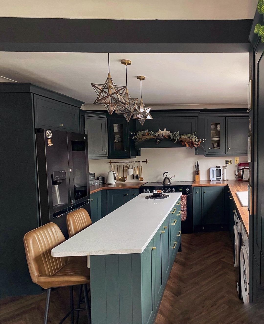 Narrow white kitchen island with brown leather stools in a dark green kitchen.