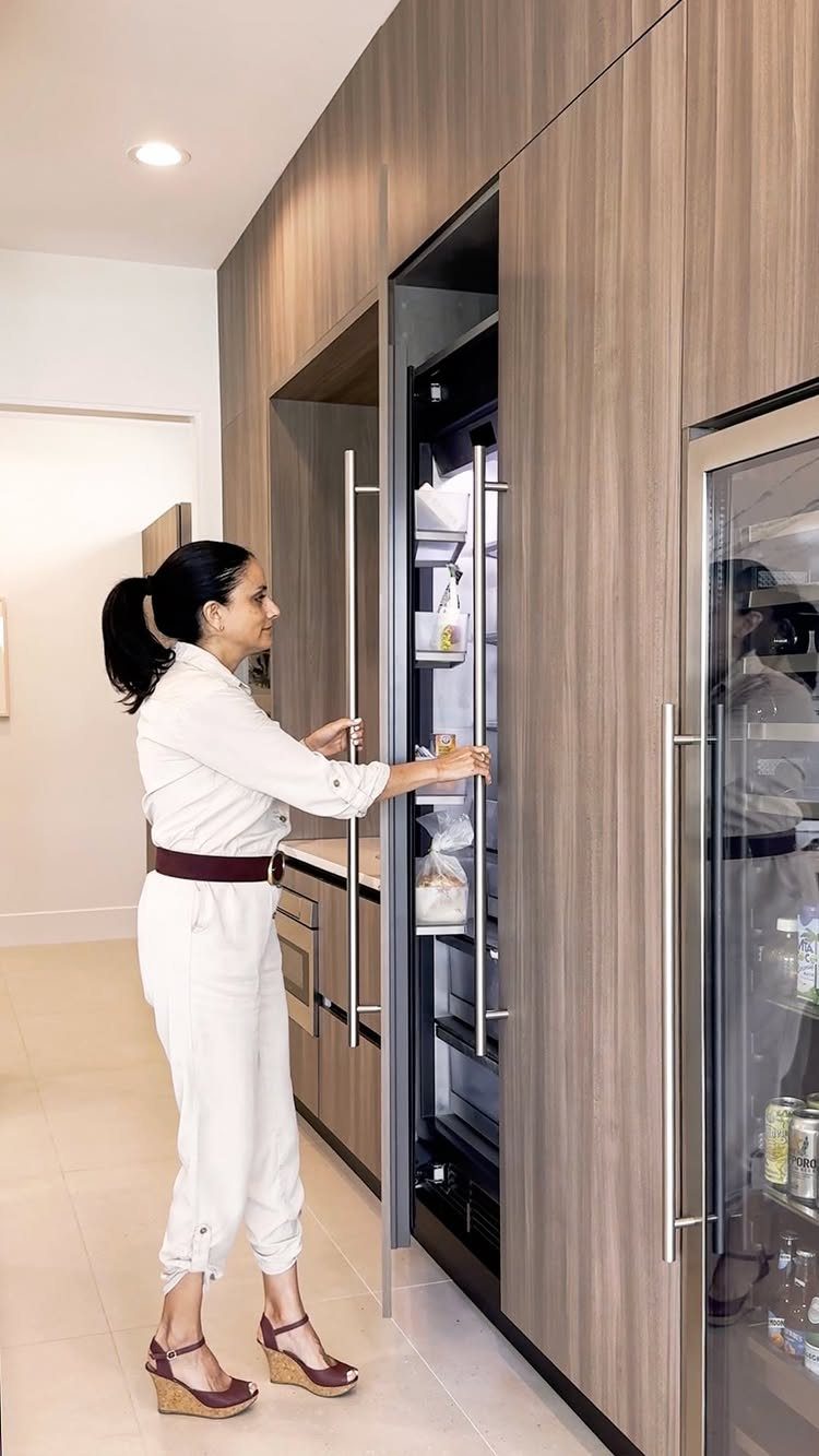 Woman opening a built-in refrigerator in a modern kitchen with light wood cabinets.