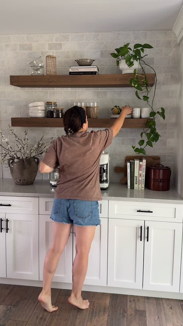Woman reaching for a dish on dark wood open shelves in a kitchen.
